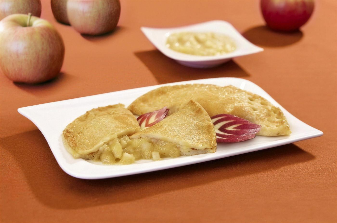 Eierpfannkuchen mit Apfelfüllung, daneben frische Äpfel und eine Schale Apfelmus